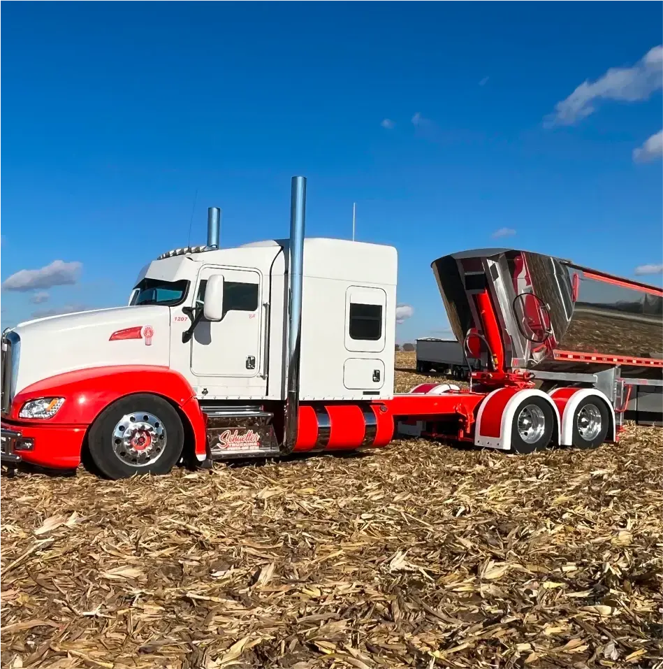 White and red semitruck with a MAC Trailer Half Round Dump attached.