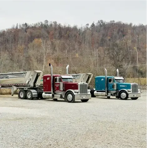 Two semitrucks side by side, both with MAC Half Round Dump Trailers attached.