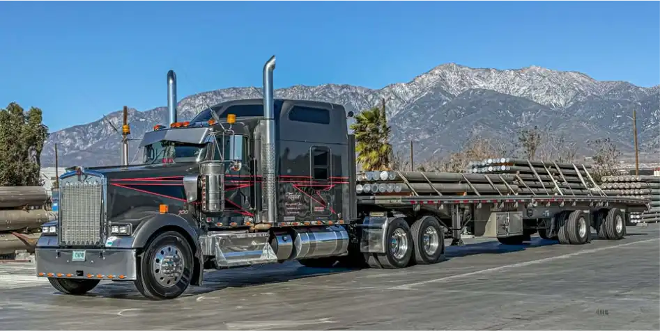 MAC Flatbed trailer loaded with metal poles. Mountains are in the background. 